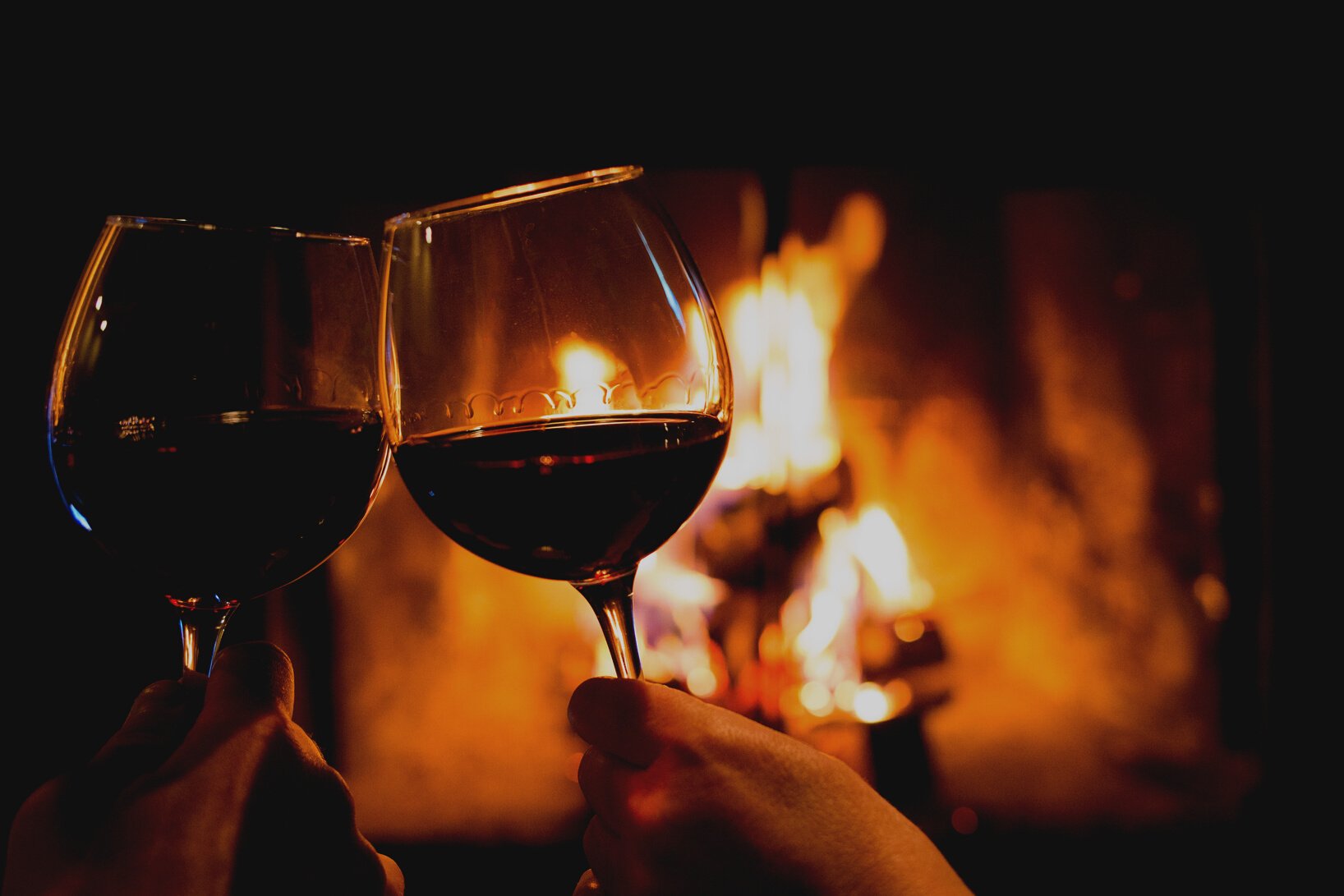 Couple holding pair of glasses with wine at fire pit